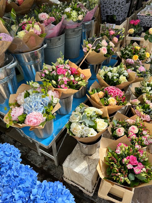 A display of fresh floral arrangements at flowerschessington.co.uk, featuring bouquets with pink, white, and blue flowers arranged in brown craft paper and metallic buckets. The arrangements include r